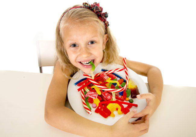 pretty happy Caucasian female child eating dish full of candy in sweet sugar abuse dangerous diet